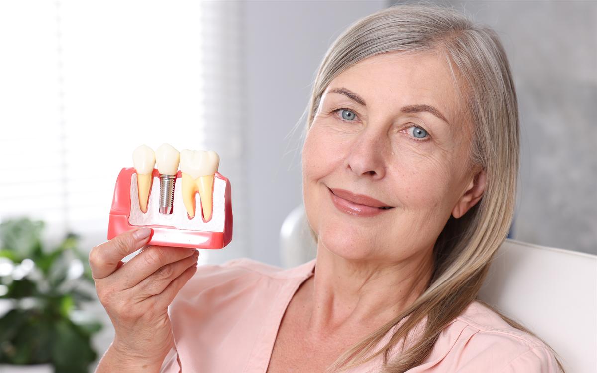 Una mujer mayor sonríe sosteniendo la maqueta de un implante dental.